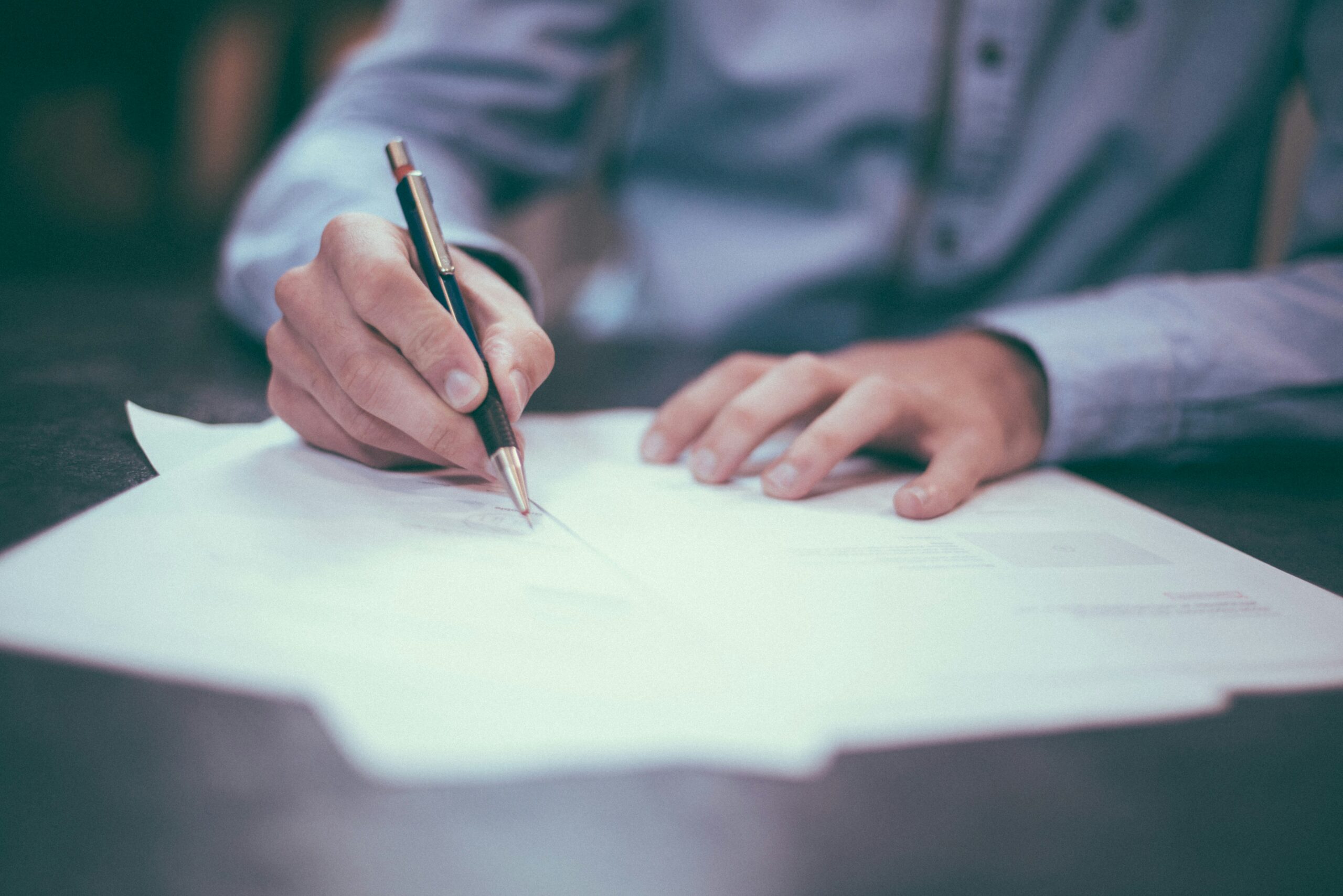 Close view of man's hands holding pen as he signs an insurance policy agreement.